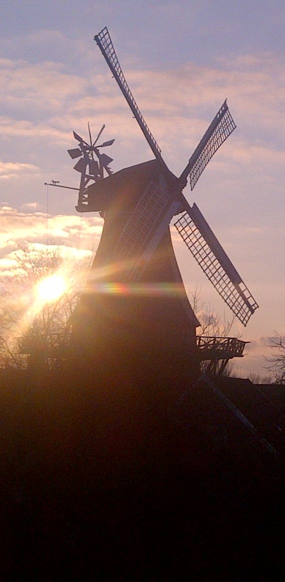 Blick aus dem Fenster von Haus Muschelgiebel Windmühle von Ditzum im Sonnenuntergang – direkt vom Haus Muschelgiebel Garten aus sichtbar, perfekt für ruhige Abendmomente
